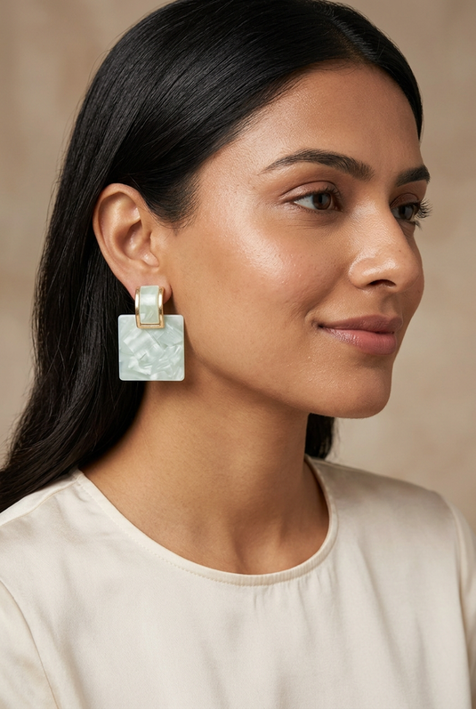 Woman in an ivory blouse wearing mint green marble-effect square drop earrings with gold-tone rectangular tops.