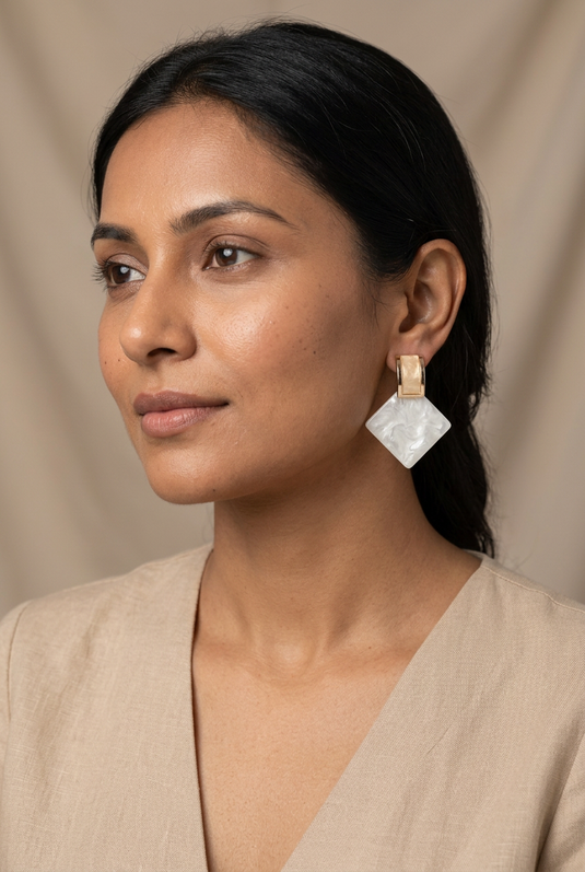 Woman in a beige blouse wearing ivory marble-effect square drop earrings with champagne-coloured gold-tone tops.