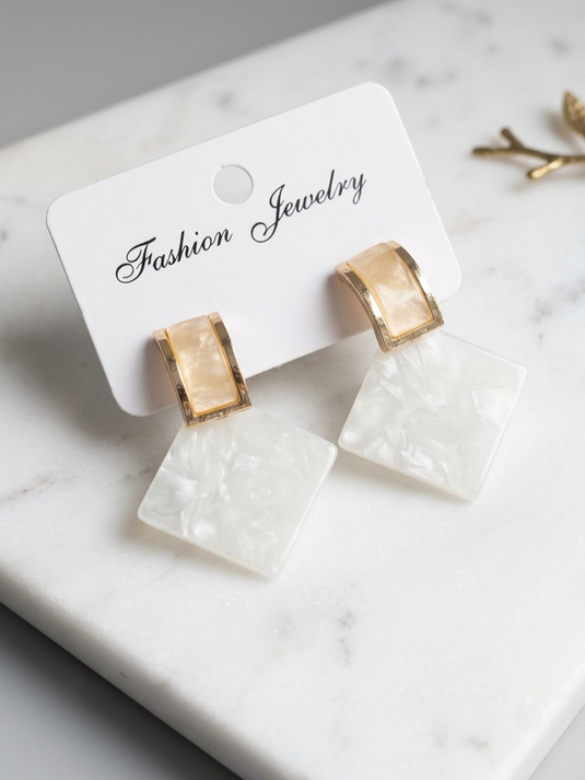 Ivory marble-effect square drop earrings with champagne-coloured tops and gold-tone frames on a display card.