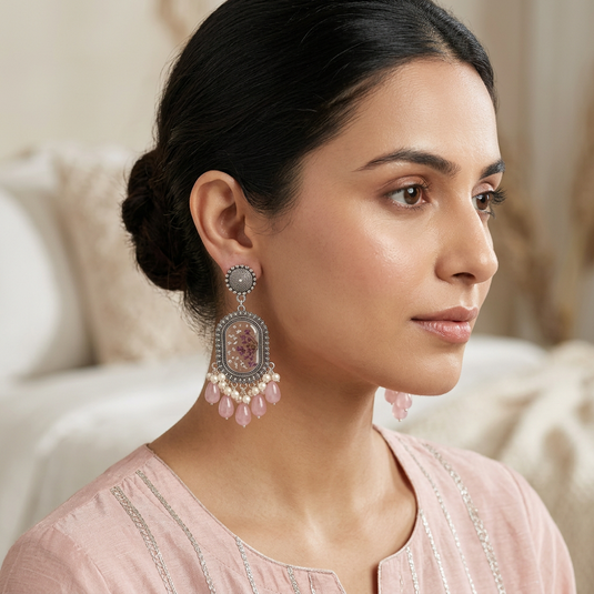 GARIMAS blush pink floral resin drop earrings worn by a woman, with ornate silver-tone frames and cream bead accents.