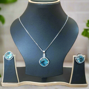 Aqua Blue Pendant Set by Garimas featuring CZ studs and silver-plated chain displayed on a jewelry stand.