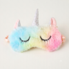 A plush unicorn sleep mask with a pastel rainbow gradient, featuring embroidered closed eyes, a silver glitter horn, and pink ears, shown on a plain light background.