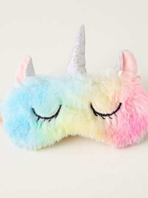 A plush unicorn sleep mask with a pastel rainbow gradient, featuring embroidered closed eyes, a silver glitter horn, and pink ears, shown on a plain light background.