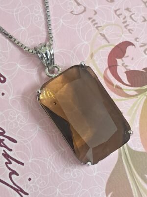 Garimas Smoky Yellow pendant with silver chain, set against a patterned background.